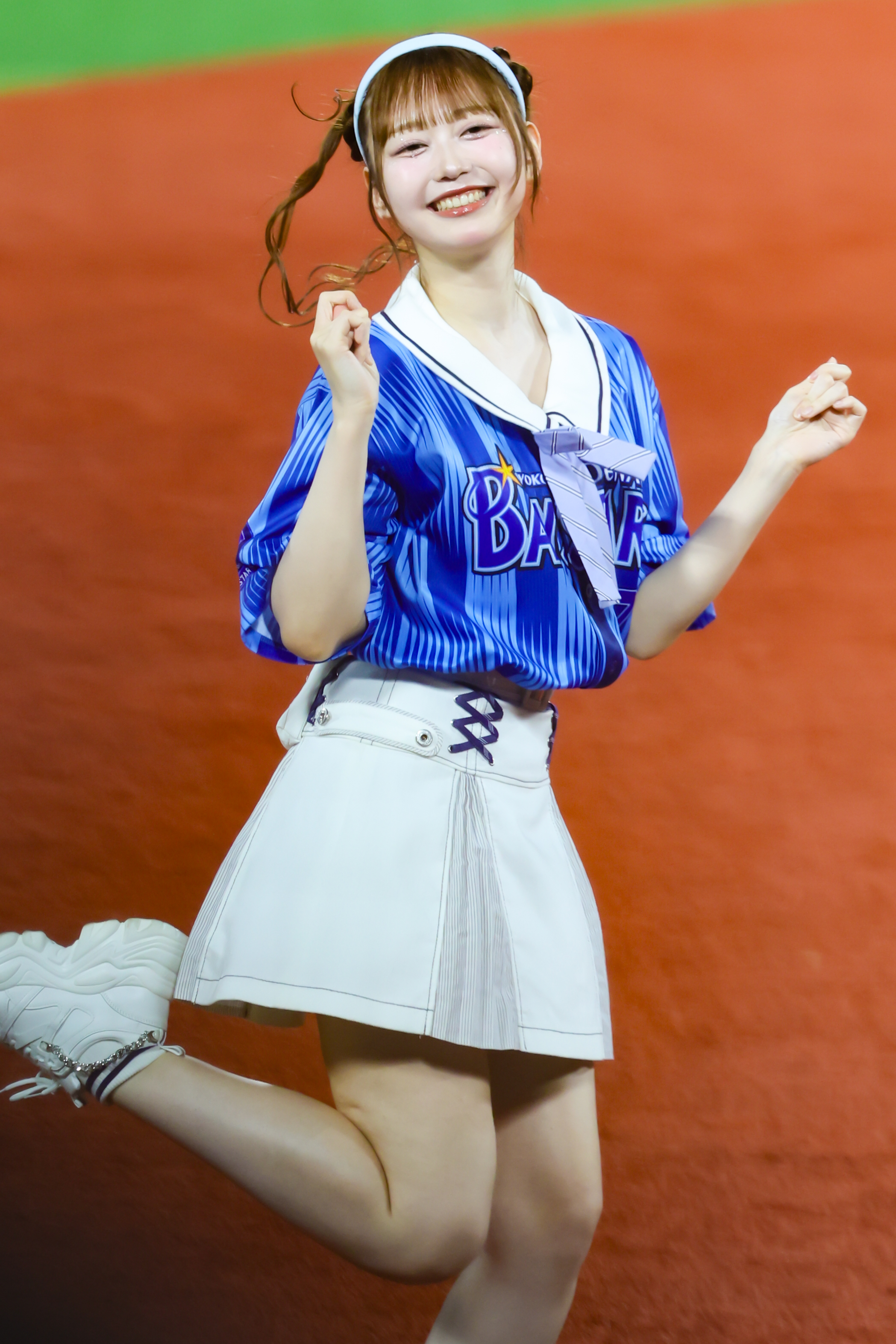 A cheerful performer in a blue team jersey and white skirt, dancing energetically on a baseball field.