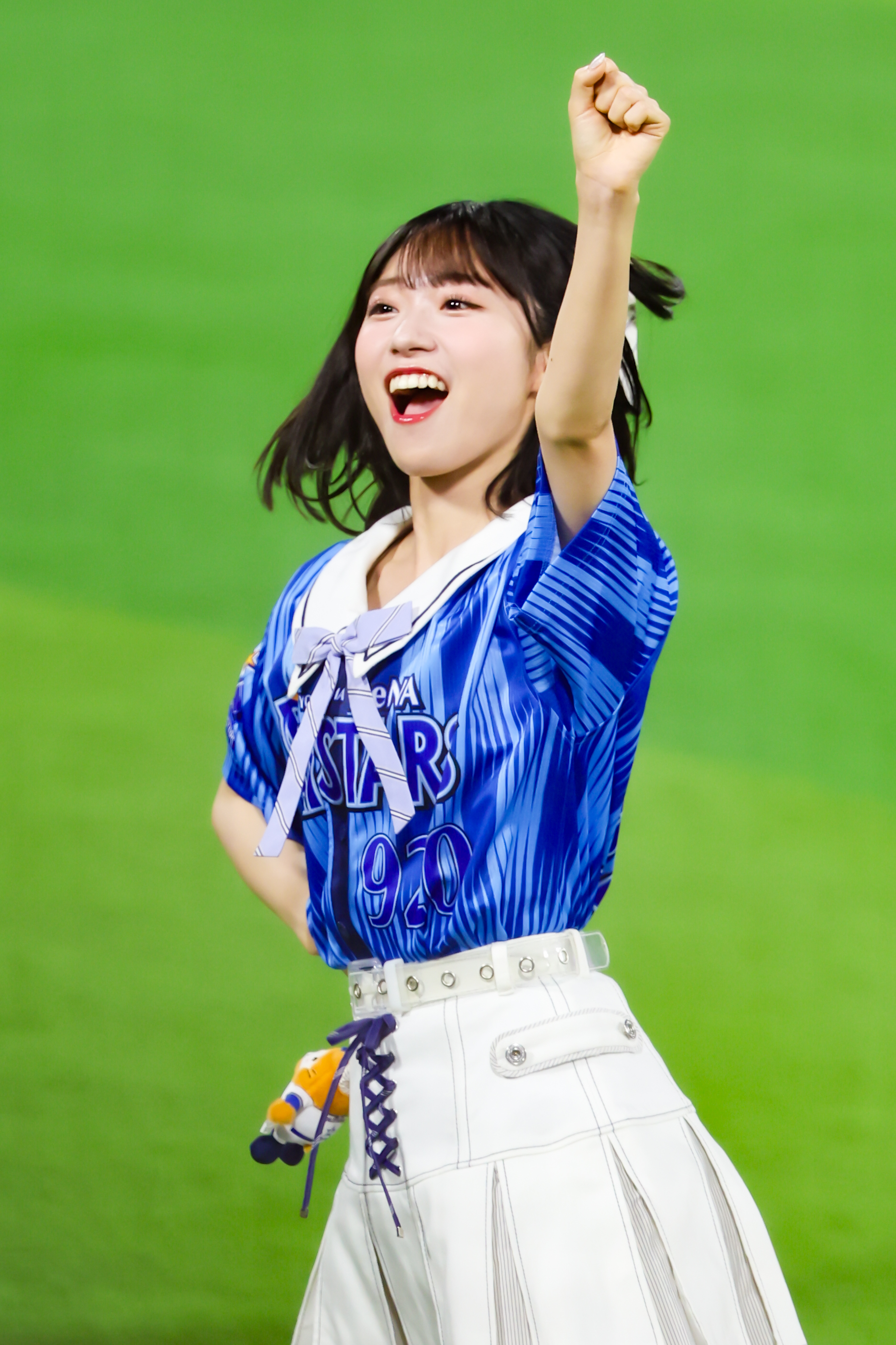 A performer wearing a blue sports jersey and white pants, joyfully raising a fist in celebration.