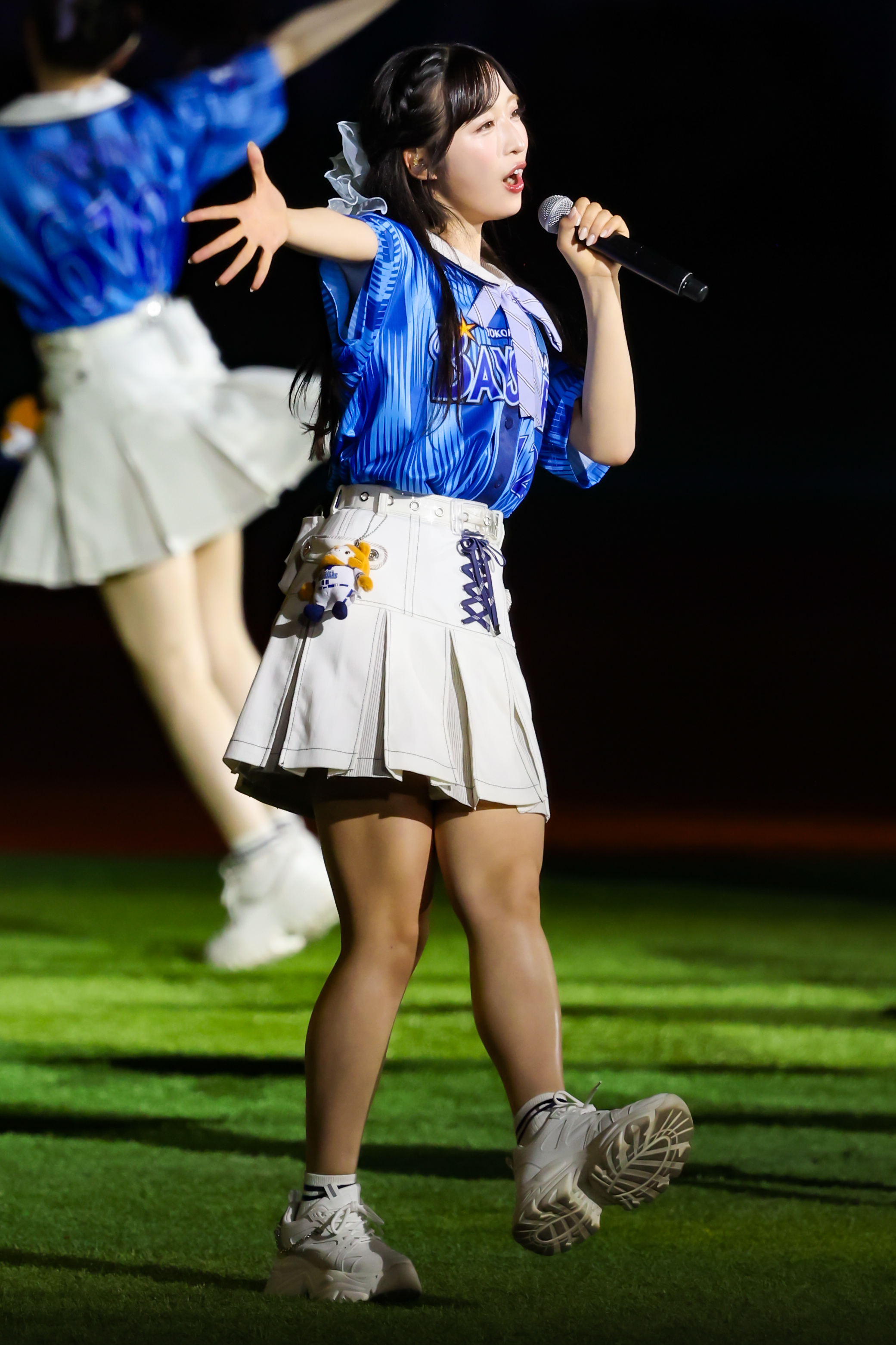 A performer wearing a blue and white outfit singing into a microphone on a stage, with a crowd in the background, highlighting excitement and energy.