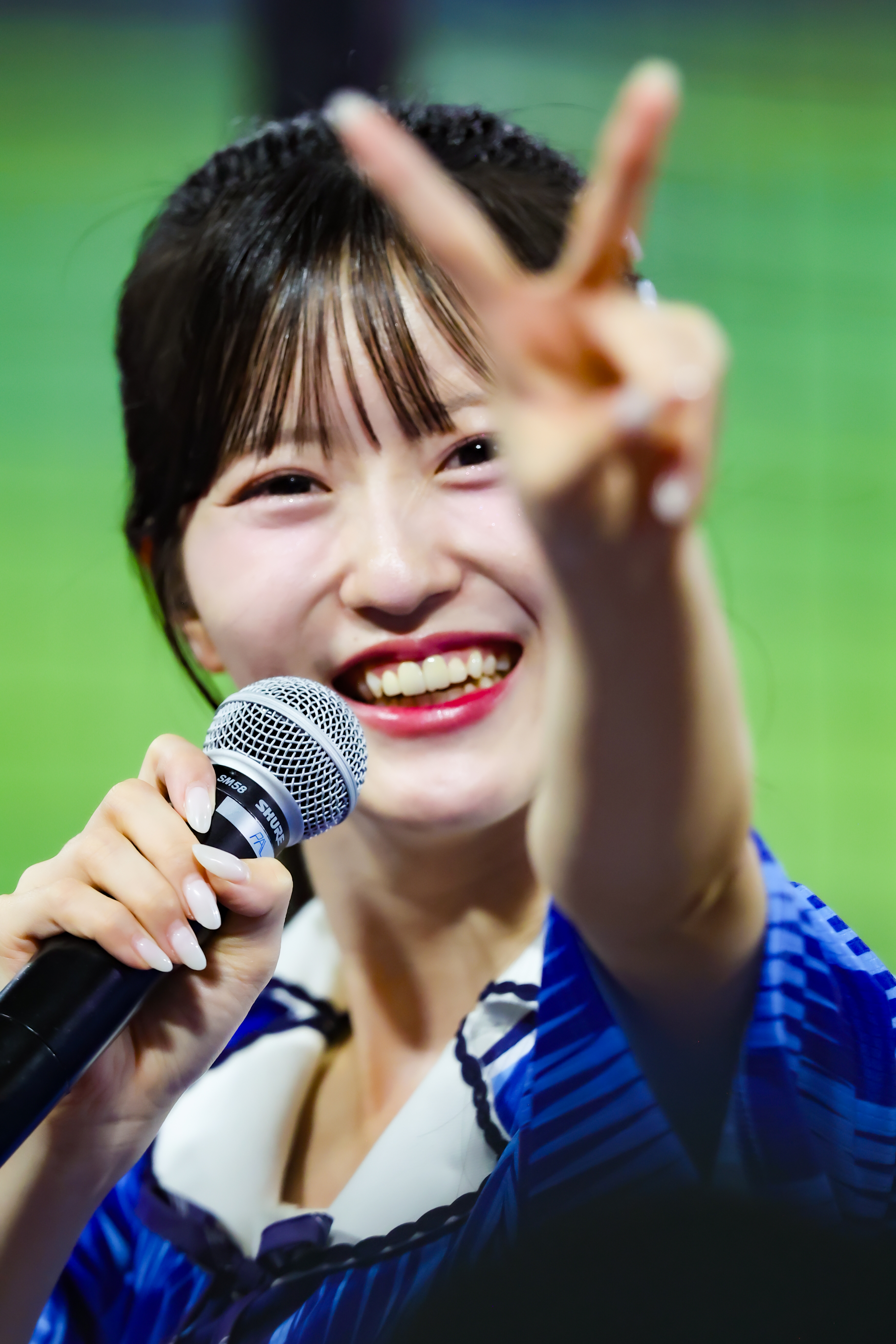 A young woman smiling widely while holding a microphone and making a peace sign with her fingers.