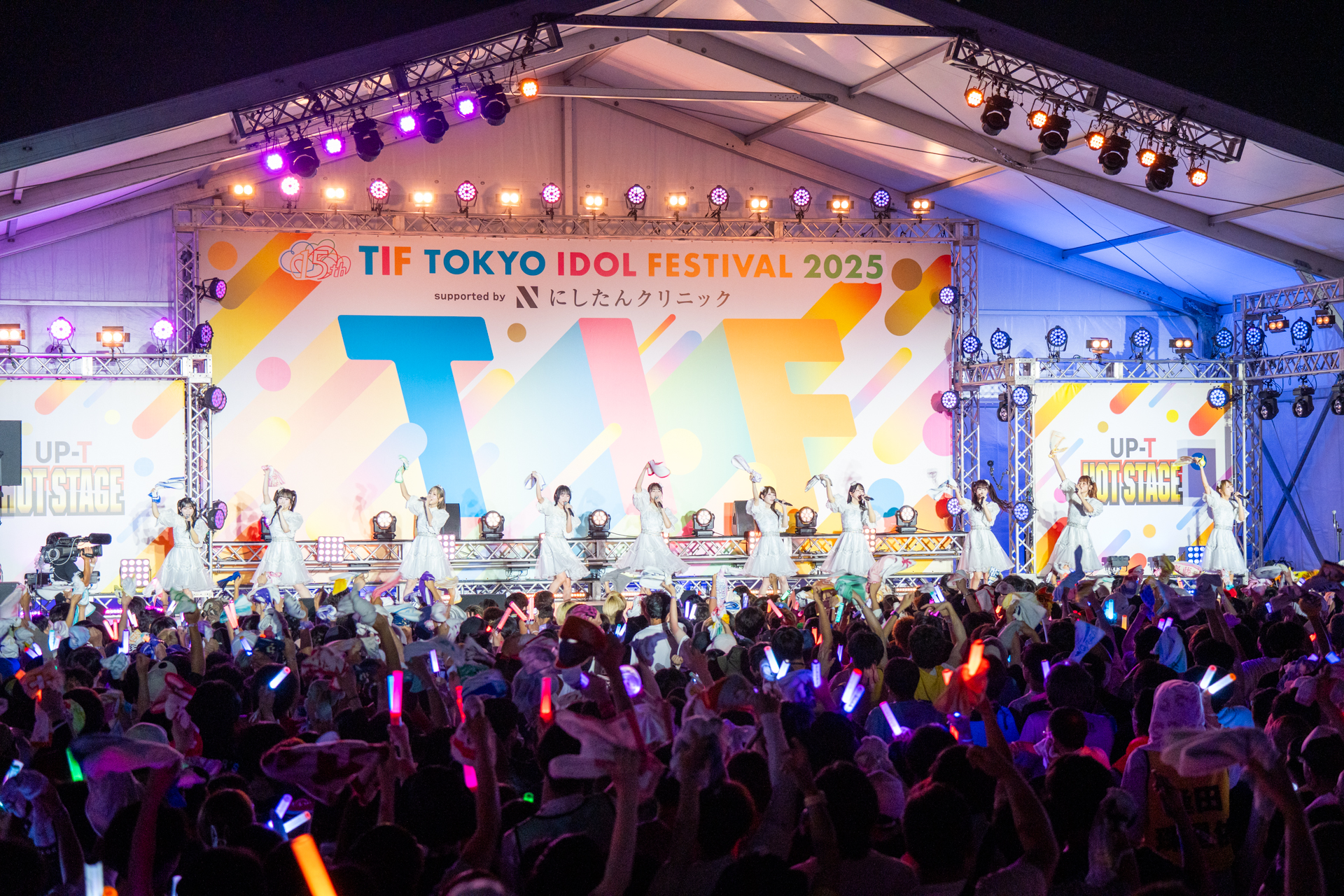 アイドルグループ＝LOVEがTOKYO IDOL FESTIVAL 2025のHOT STAGEでパフォーマンスを披露する様子。観客が盛り上がり、光るサイリウムを振っている背景に、色とりどりのステージ装飾が映えている。