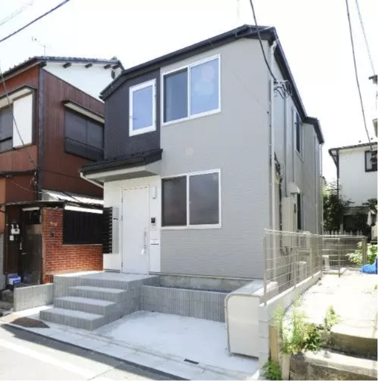 新しいデザインのシェアドアパートメントの外観。白とグレーの壁と、玄関前に階段がある。周囲には住宅が並んでいる。