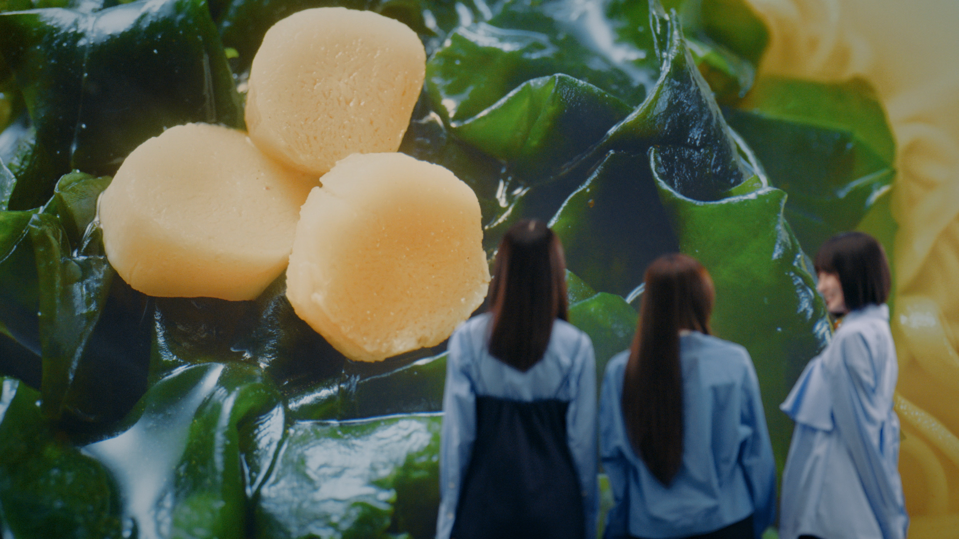 乃木坂46のメンバーが青い衣装を着て、巨大なほたて風かまぼことわかめの映像を見つめるシーン