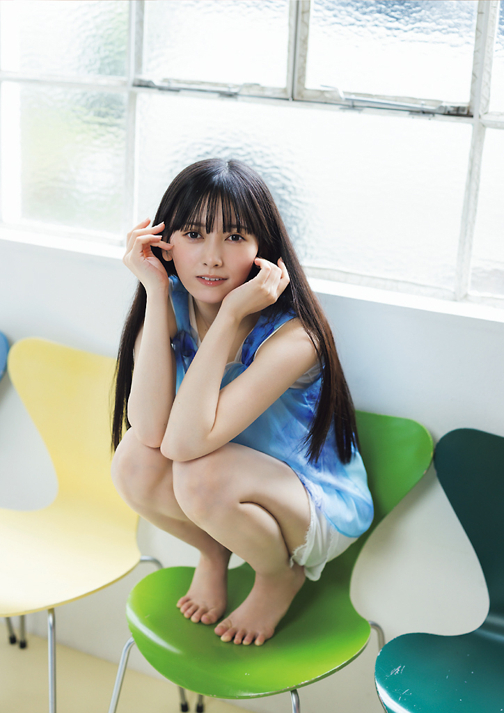 青いトップを着た女性が、カラフルな椅子の上にしゃがんで微笑んでいる。