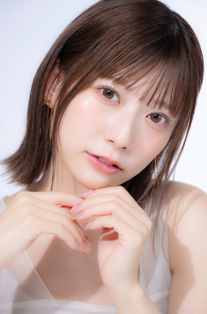 A close-up portrait of a young woman with shoulder-length brown hair, showcasing a soft expression while resting her hands near her face.